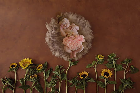 baby in pink skirt near yellow sunflowers thumbnail