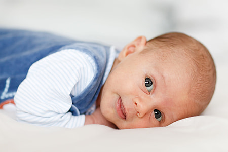 baby in blue overalls laying on white cushion thumbnail