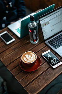 flatlay photo of coffee art latte in red ceramic mug near iPhone and MacBook Pro thumbnail
