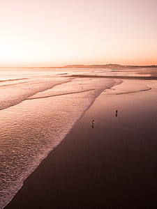 two person standing on seashore under yellowish sky thumbnail