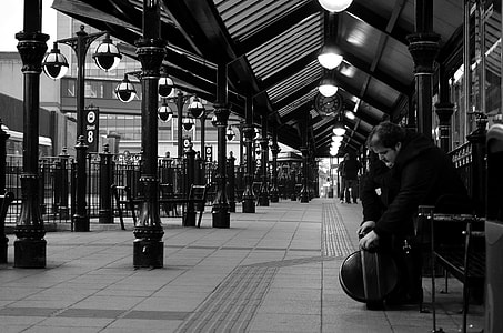 grayscale photo of man sitting down on bench outside building thumbnail