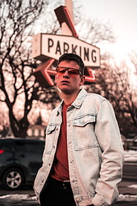 man wearing blue denim jacket standing near the parking signage thumbnail