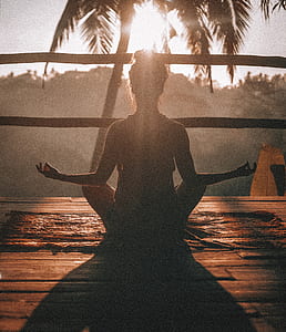 woman meditating sitting on brown rug facing sunset and trees thumbnail