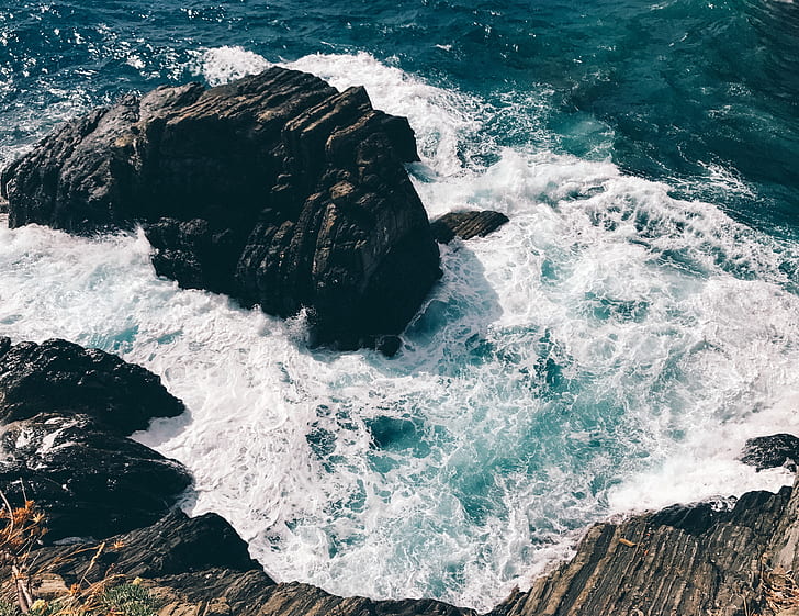 black rock formation hits sea wave at daytime