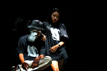 woman standing beside man sitting smoking cigarette thumbnail