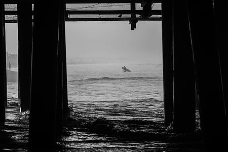 gray scale photography of person holding surfboard thumbnail
