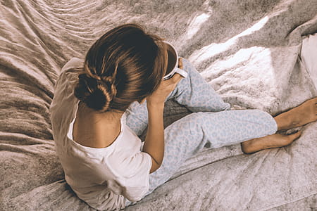 Attractive young girl in a pajamas holding a cup of tea while sitting in white bedding thumbnail