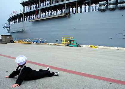 boy sitting at dock looking on a ship with marines in it thumbnail