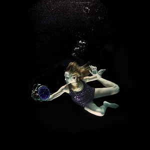 woman in purple swimsuit holding bell alarm clock underwater thumbnail