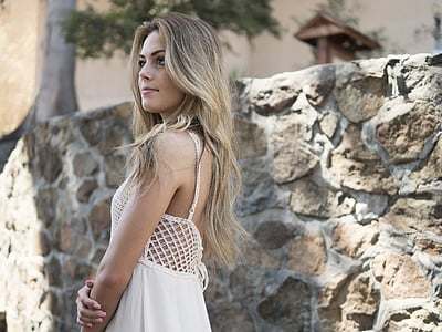 woman in white spaghetti strap dress next to gray concrete wall during daytime thumbnail