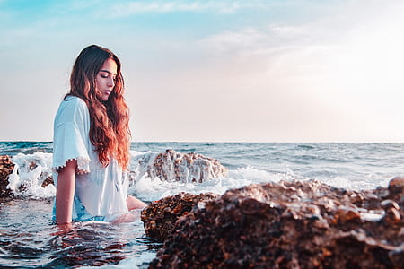 woman sitting on seashore beside stones thumbnail