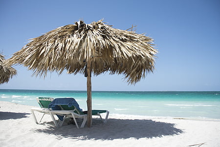 two white loungers under brown hut in front of sea during daytime thumbnail