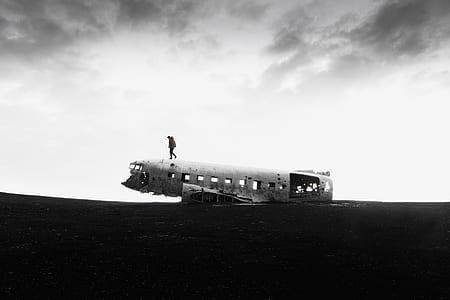 grayscale photography of person walking on crashed plane part on open field thumbnail