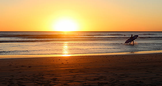 person at seashore carrying surfboard under yellow sky thumbnail