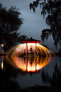 steel wool photography of person holding lights on hut above water at night time thumbnail