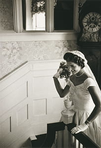 grayscale photo of woman in wedding gown standing beside stair railing thumbnail