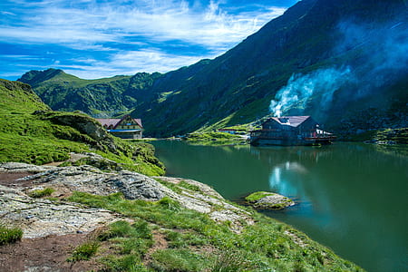 house near calm lake surrounded by mountain thumbnail