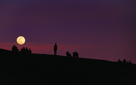 silhouette of people sitting and standing on mountain at nighttime thumbnail