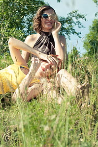 woman lying on lap of another woman sitting on grass wearing sunglasses enjoying the sunlight thumbnail