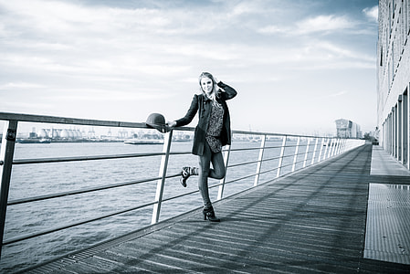 grayscale photography of woman standing beside railings thumbnail