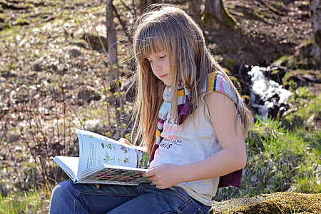 girl sitting while reading book during daytime thumbnail