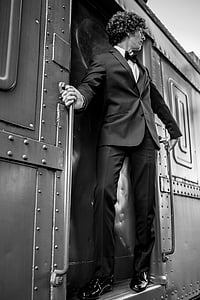 man sanding outside train door in greyscale photography thumbnail