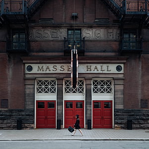 woman walking on sidewalk in front of Massey Hall during daytime thumbnail