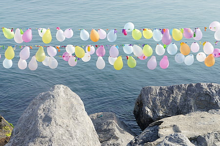 balloon buntings over stone edge and ocean during day thumbnail