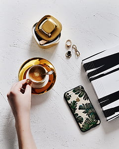 selective focus photography of cup of coffee beside phone on white surface thumbnail