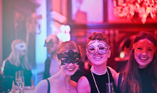 Three Young Women In Masks Posing While Holding Wine Glasses In Nightclub thumbnail