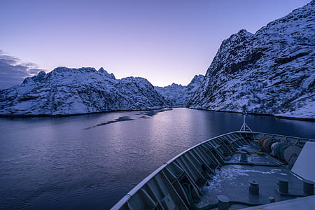 gray boat on body of water near mountain covered by snow thumbnail