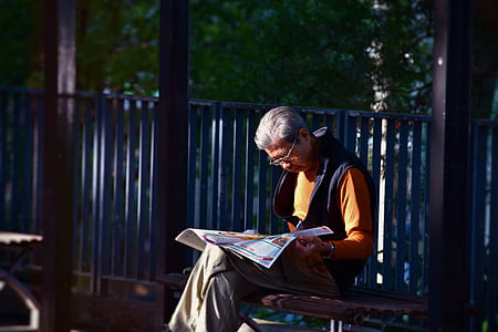 man in orange top and black vest reading paper thumbnail