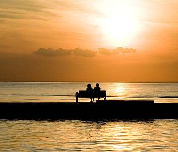 silhouette of two person sitting on bench near body of water during daytime thumbnail