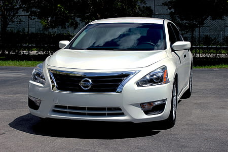 white Nissan sedan parked near trees thumbnail