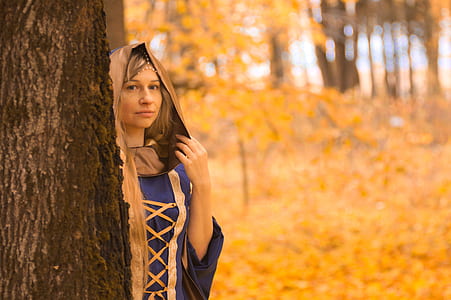 woman wearing dress with hood behind brown tree trunk closeup photo thumbnail