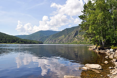 calm body of water beside trees near mountain thumbnail