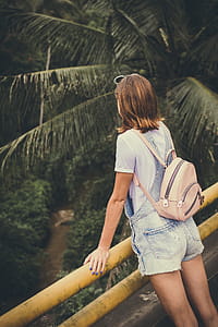 Woman Wearing Dungaree Shorts Stands Near a Yellow Metal Rail Overlook a River Belo With Coconut Trees at Daytime thumbnail