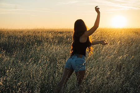 woman standing in grass field while raising right hand during sunset thumbnail