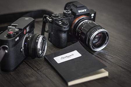 selective focus photography of two black Sony DSLR cameras both on brown wooden surface thumbnail