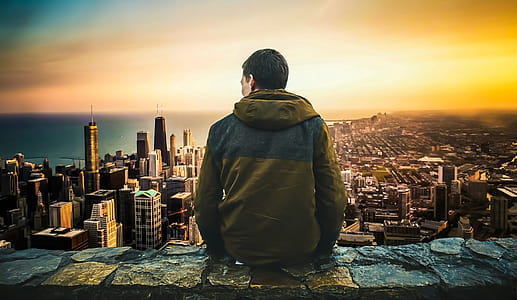 Man sitting at the edge of a tall stone landing, overlooking a modern city. thumbnail