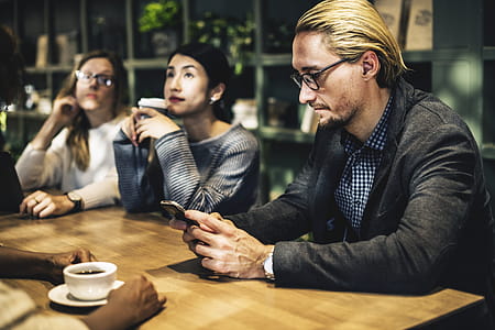 Man in Black Suit Jacket Holding Smartphone Sitting in Front of Table thumbnail