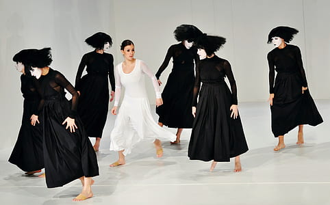 woman wearing white scoop-neck long-sleeved dress and group of woman wearing black long-sleeved dresses standing on white floor thumbnail