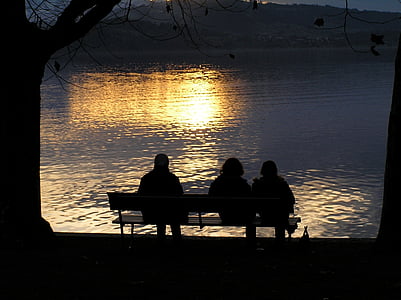 three people sitting on bench near lake thumbnail