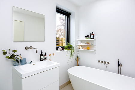 vacant white enamel bathtub beside white wooden combo sink and clear glass window thumbnail