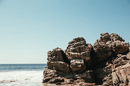 Waves crash against a large rock on the beach thumbnail