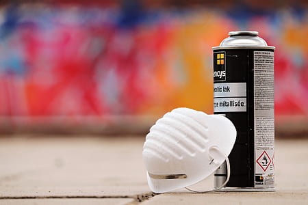 selective focus photo of white face mask and spray paint bottle on top of beige surface thumbnail