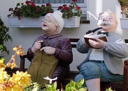 statue of woman wearing brown dress sitting beside man wearing gray jacket with black bowtie thumbnail
