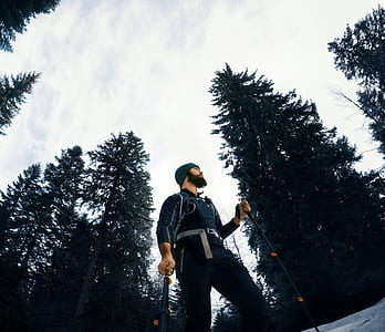 low-angle photography of man holding ski pole surrounded with trees thumbnail