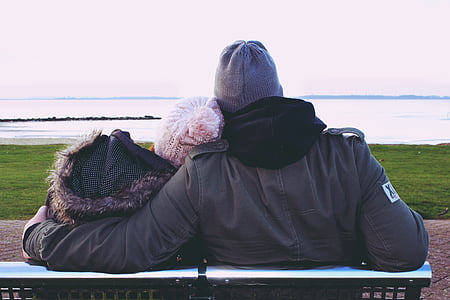 man and woman sitting while facing body of water thumbnail