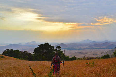 man holding sphere on brown grass field near woods and mountain under white clouds blue skies golden hour thumbnail
